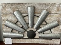 Photo showing the windmill-shaped metal wall hanging mounted on distressed wood background.