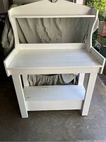 Front view of the painted white wooden potting table showing working surface, folded-up back panel, and lower storage shelf.