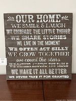 Front view of square wood wall hanging with white text featuring inspirational home quotes.