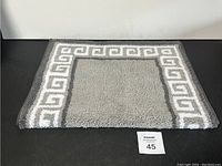 Top view of gray and white bathroom mat showing the Greek key border design.