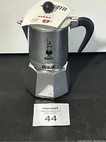 Front view of Bialetti 3 cup stovetop espresso maker with label on lid and black plastic handle.