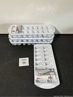 Four white plastic ice cube trays stacked, showing one tray separately in front with packaging label.