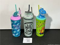 Three kids straw cups with decorative lids displayed side by side showing the different animal and character themes and color schemes.