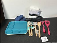 Photo showing turquoise plastic serving tray with multiple compartments, 4 wooden handled spatulas with animal designs, 2 blue oven mitts, 3 additional spatulas and a black slotted spoon.