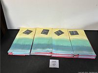 Four folded kitchen towels laid flat, showing the gradient yellow-green-blue color with red trim.