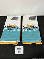 Two packs of kitchen towels folded with visible patterned towels featuring 'Summer Vibes' text and sun graphic on turquoise background, with yellow towels underneath.