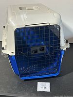 Front view of a small plastic pet carrier with blue base, white top, and black metal wire door with latches.