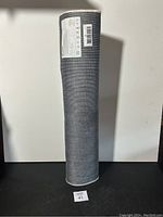 Full view of the rolled rug runner standing upright, showing the textured gray fabric and a white edge binding.