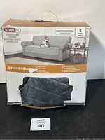 Photo of boxed Smart Fit sofa cover set with some parts displayed outside the box showing gray quilted plush fabric.