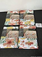 Lot of four floral print tablecloths packaged, showing various sizes and price labels.