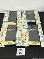 Four folded Hometrends brand tablecloths with floral pattern and packaging labels showing dimensions.