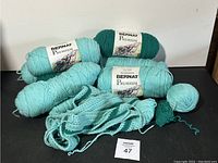 Six skeins of Bernat Premium yarn and some fabric pieces shown together on white background