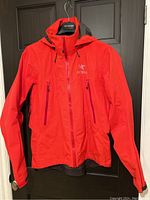 Front view of red Arc’teryx jacket showing full-length zipper, two zippered chest pockets, and logo