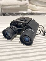 Front view of compact 8x21 binoculars showing objective lenses and neck strap.