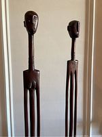 Front view of two tall carved wooden sculptures side by side.