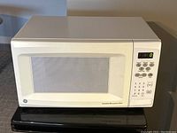 Front view of white GE turntable microwave oven with control panel and door with mesh window visible.