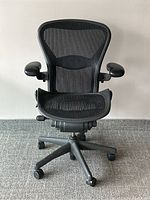 Front view of black mesh office chair on caster base, showing seat, back and adjustable armrests