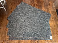 Four new large charcoal Marathon branded industrial doormats laid overlapping on hardwood floor.
