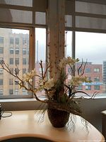 Full view of large artificial silk flower arrangement with cream flowers and tall branches on desk near window.
