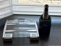 Front angle shot of the glass digital bathroom scale beside the Braun shaver in its charging station.
