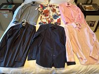 All 11 men's dress shirts displayed on bed in two groups showing variety of colors, styles, and conditions