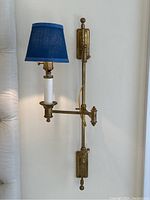 Full view of one brass wall sconce lamp mounted on wall with blue shade