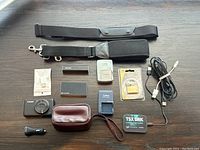 Overview of lot items laid out on table: straps, chargers, battery packs, camera, case, cables, padlock and card