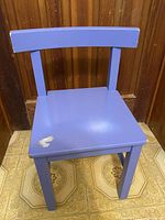Front view of blue vintage child's wooden chair showing seat and backrest with paint chipping on the seat front corner.