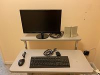 Photo showing the monitor on a black round base with cables, speakers beside it, keyboard and wired mouse on a table underneath.