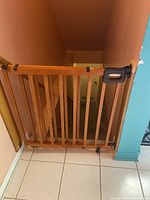 Wooden baby gate installed in a doorway with adjustable width, vertical slats, latch handle in place, securing a stairway opening.