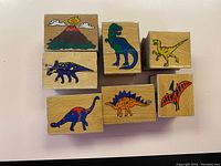 Photo of 7 wooden rubber stamps with colorful dinosaur and volcano images on one side.