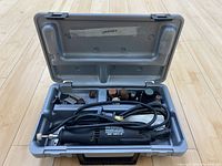 Open Dremel 3950 case showing the rotary tool unit and various accessory bits arranged in designated spaces inside the gray molded plastic interior.