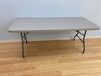 Full view of the extended Staples folding table with light gray plastic top and metal legs on wooden floor.