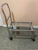 Photo of silver-colored metal dolly with two wire mesh trays and handle, showing condition and wheels.