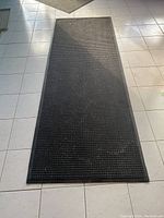 Large black rubber-backed entrance mat with grid surface pattern laid on tiled floor
