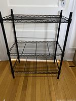 Full view of the black metal shelving unit showing three wireframe shelves and the adjustable frame.