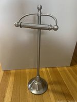 Freestanding brushed steel toilet paper holder with round base and holder for extra rolls shown upright against white background.