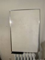 Photo of large whiteboard with silver aluminum frame and attached black marker tray at the bottom. Board surface shows slight faint marker marks.
