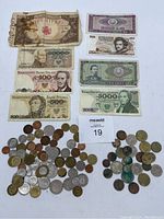 The full view of the assorted foreign paper money and numerous coins arranged around a lot number card.