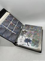 Open black binder showing multiple plastic pages filled with Marvel and DC comics collectible cards, featuring characters such as Venom, Green Lantern, and more.