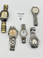 Top-down view of five men's wristwatches showing various metallic bands and dial designs.