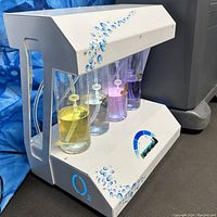 Front-left perspective of white infusion stand showing water droplet decals and four colored aroma bottles