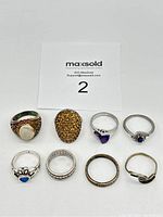 Photo capturing the full lot of 8 sterling silver rings arranged in rows, showing variety in design and stone colors.