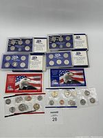Overview of all six US Mint coin sets including 2003 and 2005 uncirculated and proof sets with packaging featuring US flag and eagle images and coins sealed in plastic holders.