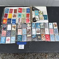 Photo showing approximately 48 decks of vintage airline-themed playing cards stored in a worn plastic-sleeve binder, laid out on table. Cards show various airline logos and colorful designs.