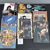 Top down view of all 11 vintage music songbooks showing a variety of covers including Michael Jackson, Prince, USA for Africa, and The Wiz.