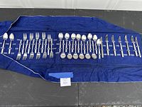 Wide shot of entire United Airlines flatware set on blue cloth showing all forks, spoons, knives in one view.