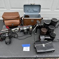 Full lot overview showing cameras, lens cases, camera bags, tripod, and camera accessories on table