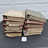 Two stacks of closed scrapbooks showing various covers including beige, red and textured covers.
