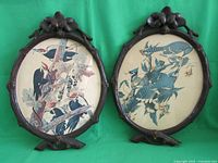 Two oval Black Forest carved frames showing woodpecker and bluejay prints side by side on a green background
